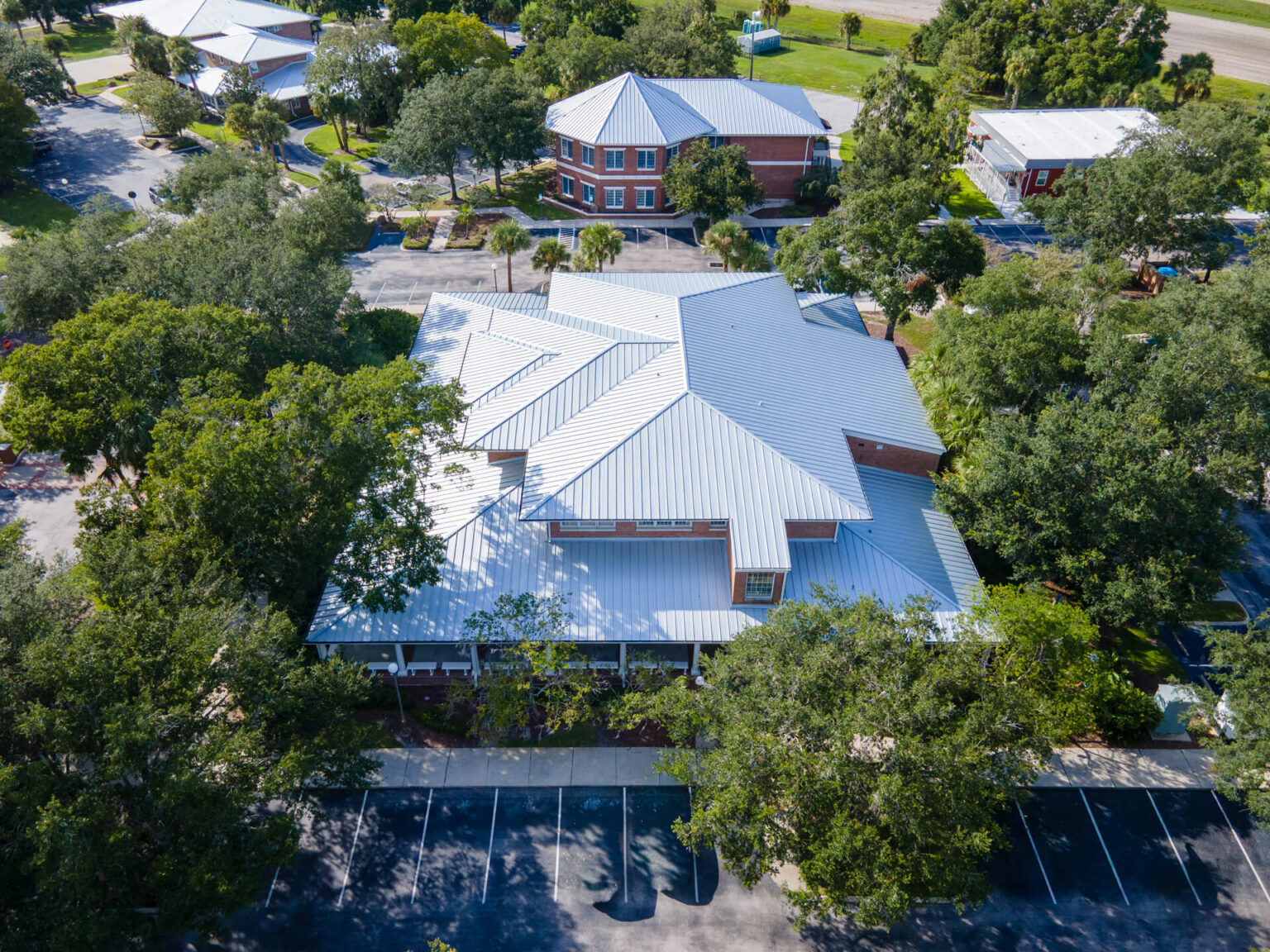 Aerial view of a commercial building with a modern metal roof surrounded by trees and parking spaces, highlighting quality roofing work by Central Florida Equity Builders.