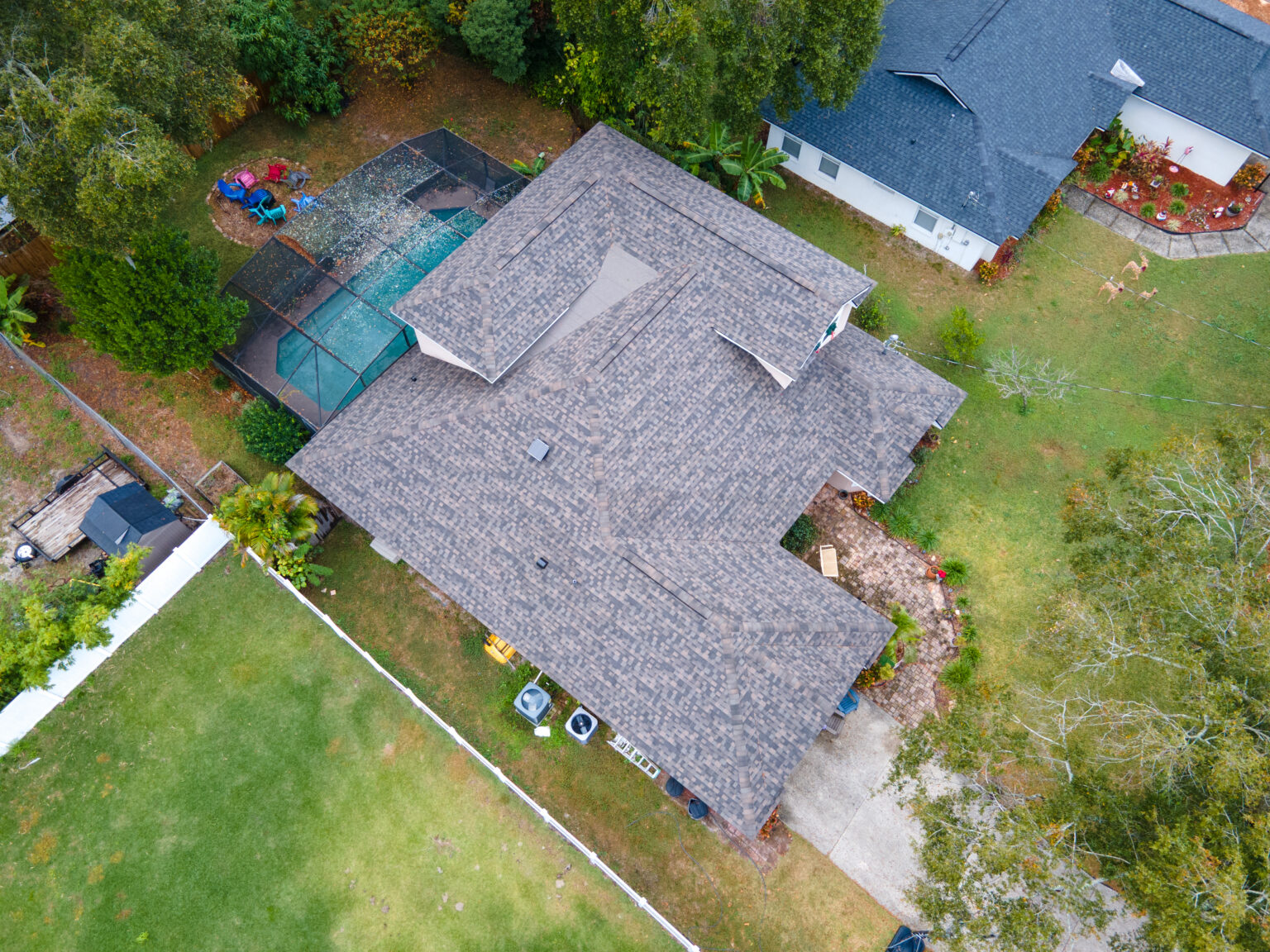 Aerial view of a residential roof in Central Florida, showcasing a well-maintained shingle roof, adjacent backyard with pool enclosure, and surrounding green lawn, relevant to storm damage repair services.